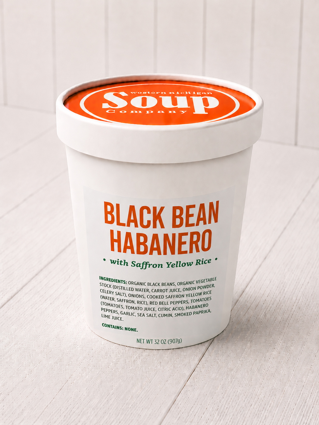 Container of Black Bean Habanero soup with saffron yellow rice on a light wooden surface.