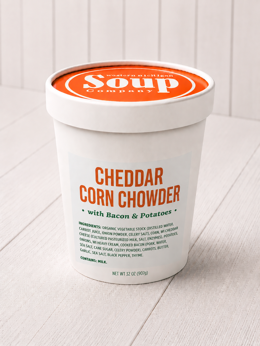 Container of cheddar corn chowder with bacon and potatoes on a white surface