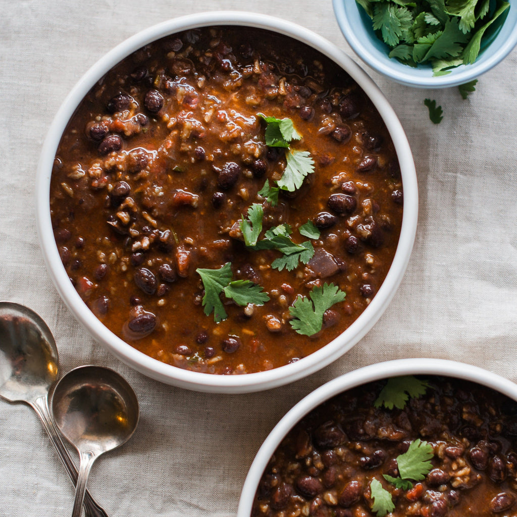 Two bowls of Black Bean Habanero soup on a table with spoons and cilantro garnish.