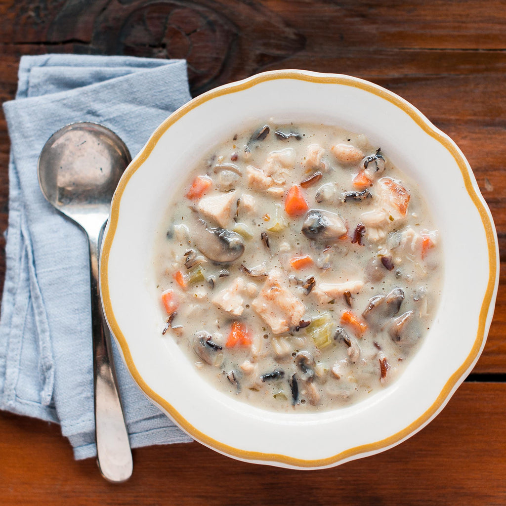 A bowl of Blackened Chicken Wild Rice soup with a spoon on the side, placed on a wooden table.