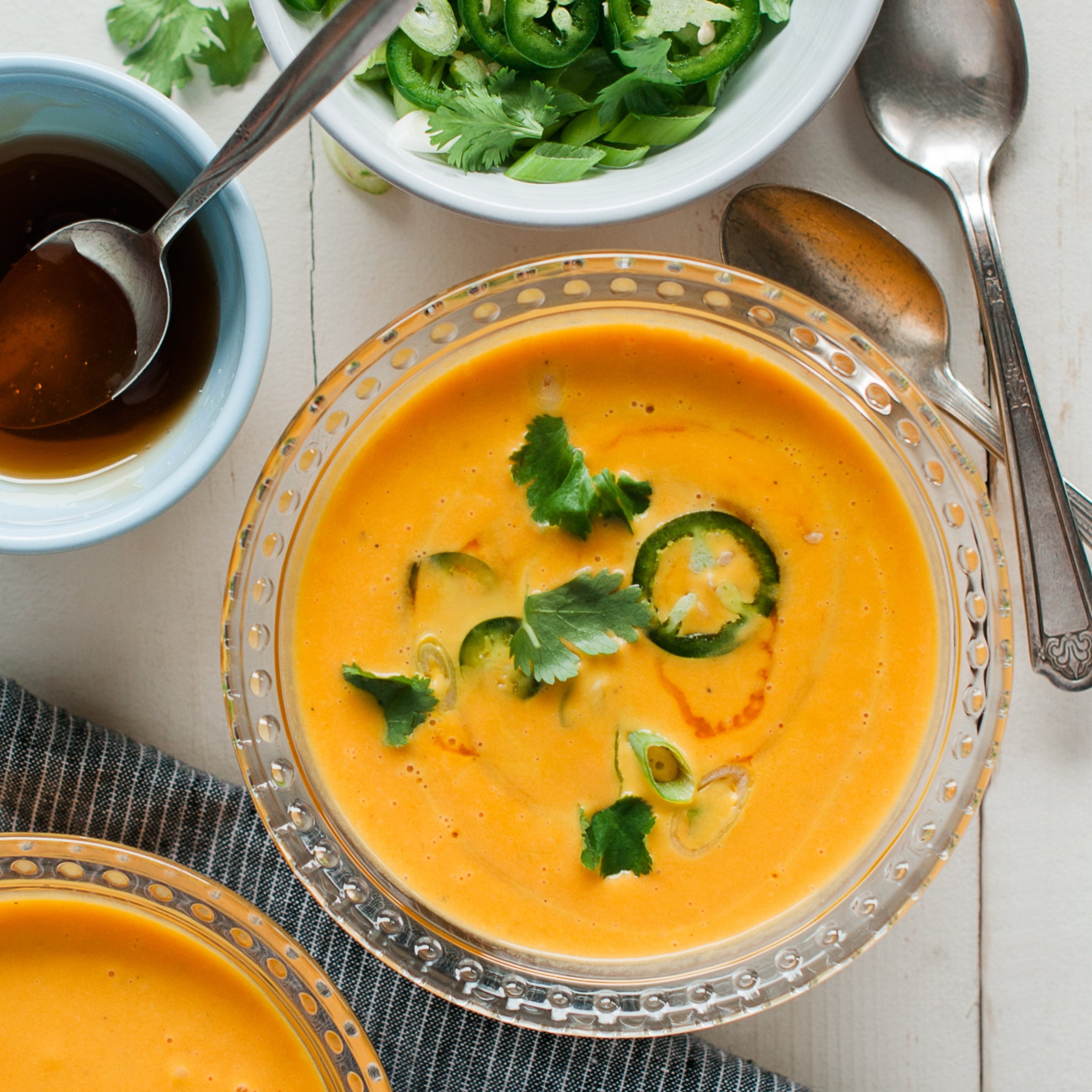 A bowl of carrot and ginger soup garnished with green onions, with a side salad and utensils on the side.