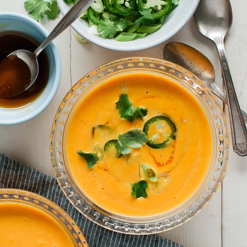 A bowl of carrot and ginger soup garnished with green onions, with a side salad and utensils on the side.