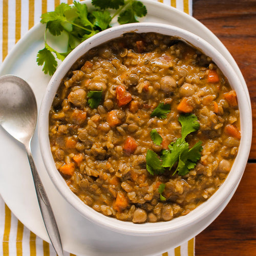 A bowl of curry lentil soup with chickpeas, basmati rice, and diced vegetables, garnished with fresh cilantro.