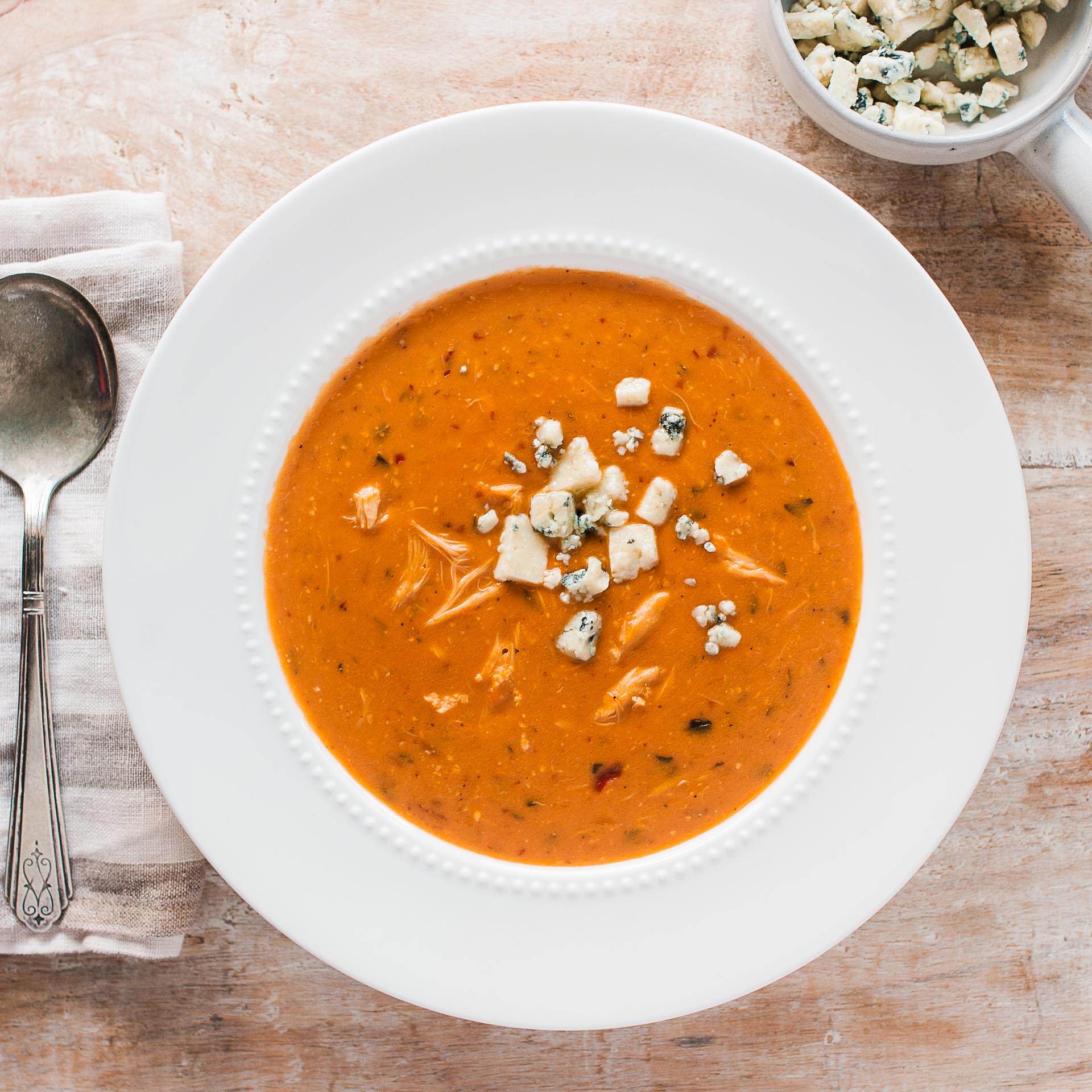 A bowl of Gorgonzola Crab Bisque topped with crumbled gorgonzola cheese and fresh basil, with a spoon on the side.