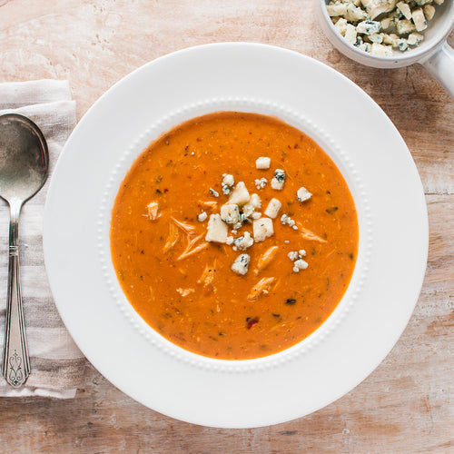 A bowl of Gorgonzola Crab Bisque topped with crumbled gorgonzola cheese and fresh basil, with a spoon on the side.