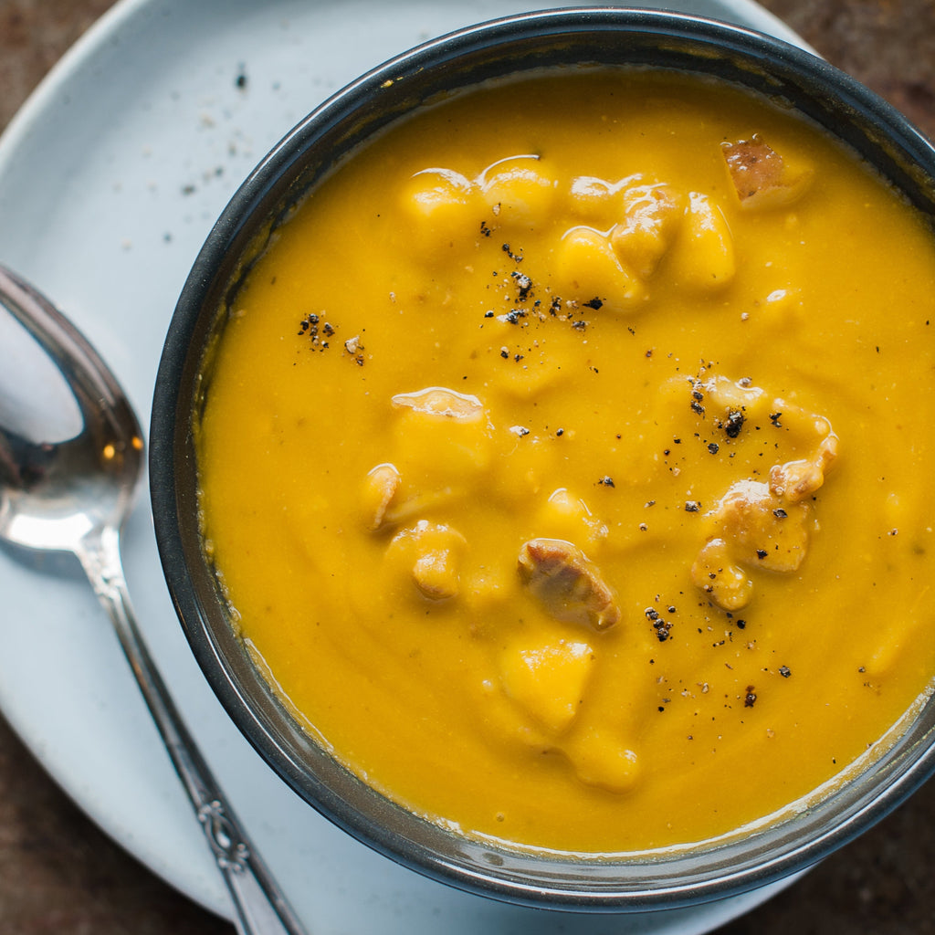 A bowl of Harvest Split Pea soup with visible chunks of potato and bacon, garnished with black pepper.