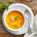 A bowl of lobster bisque soup garnished with parsley, with a spoon on the side, on a wooden table.