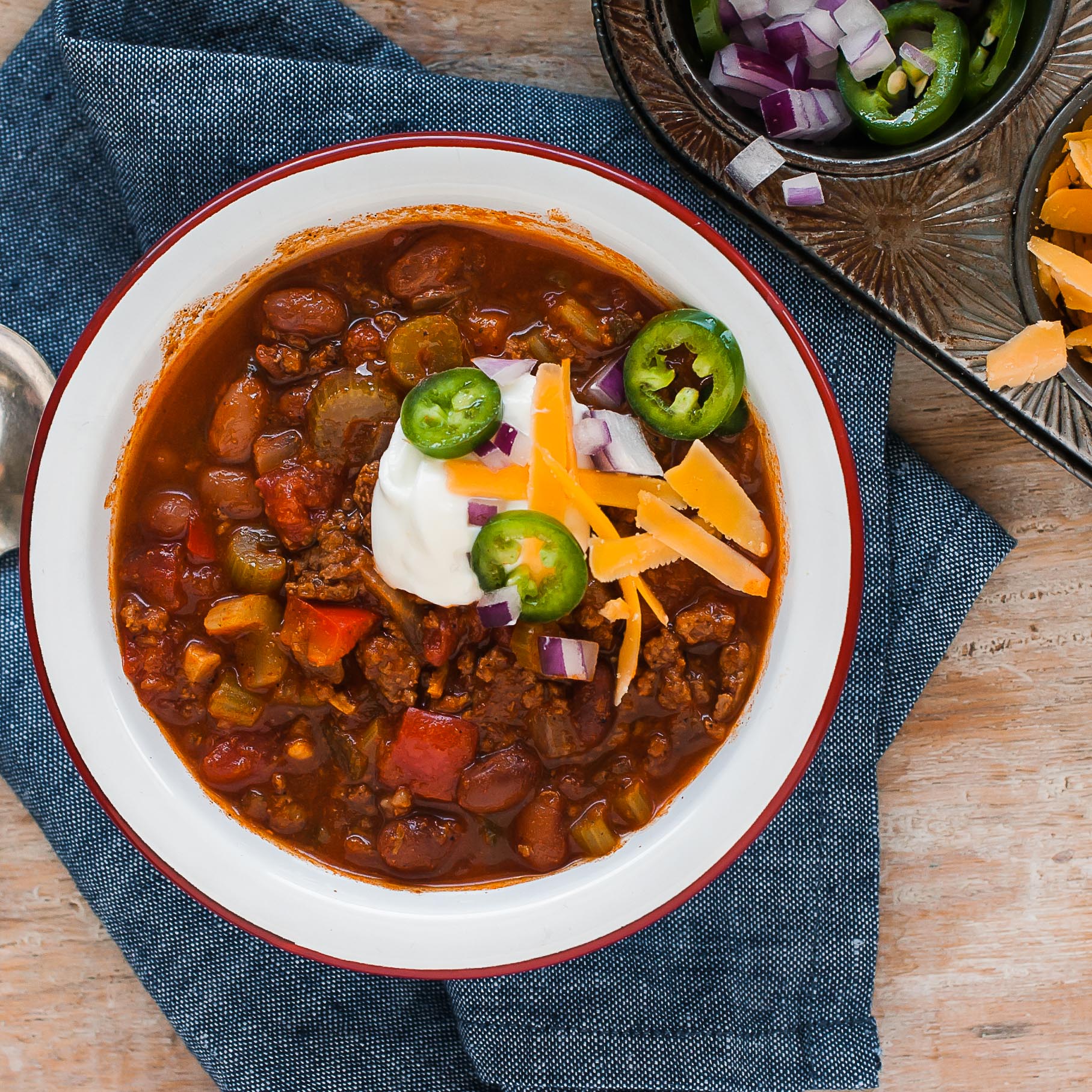A bowl of Mom's Chili with ground beef, kidney beans, and vegetables, garnished with sour cream, cheese, and jalapenos.