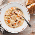 A bowl of Smoked Kielbasa & Cabbage soup with a spoon, alongside pieces of bread, on a wooden surface.