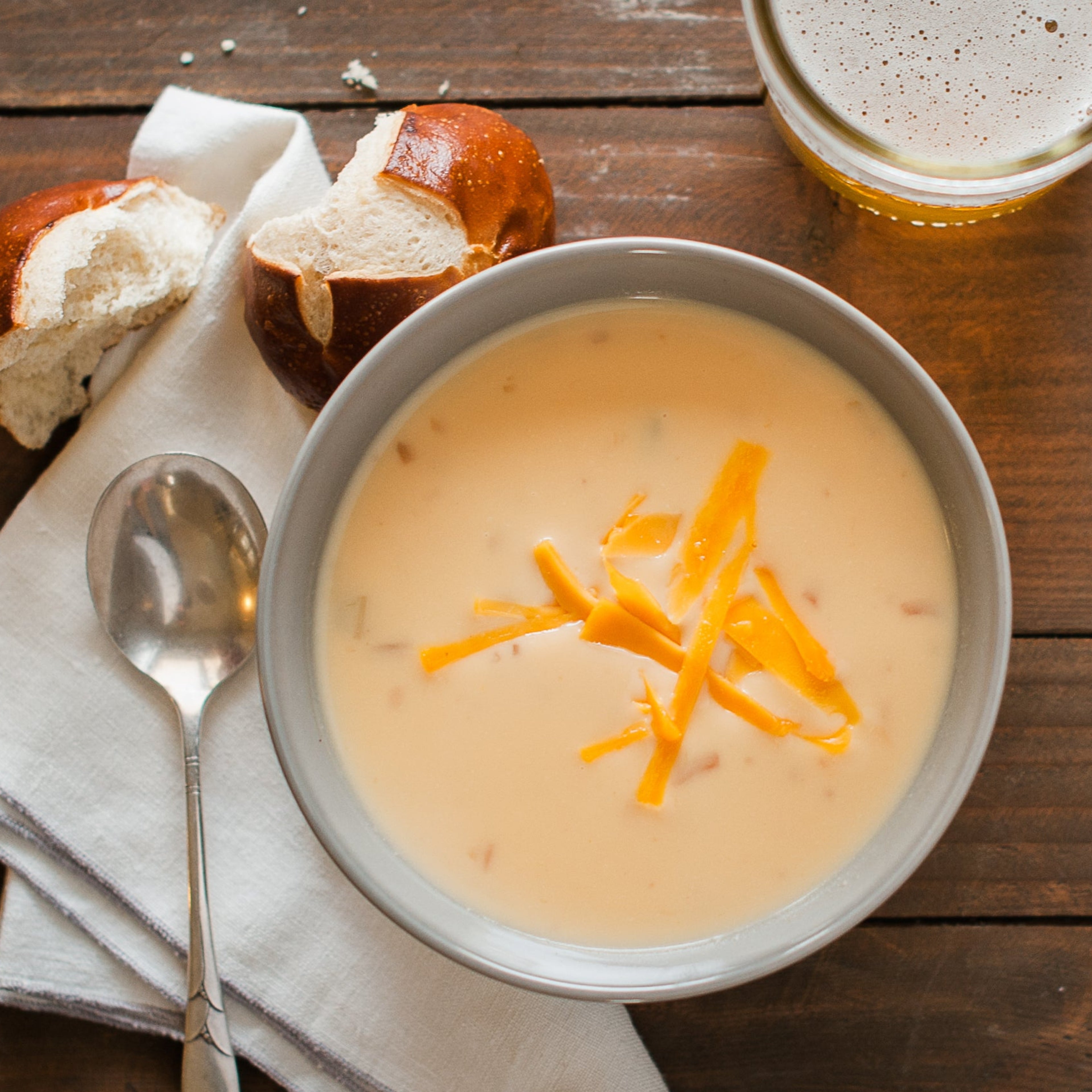 A bowl of Wisconsin Beer Cheese soup with shredded cheese on top, served alongside bread and a glass of beer.