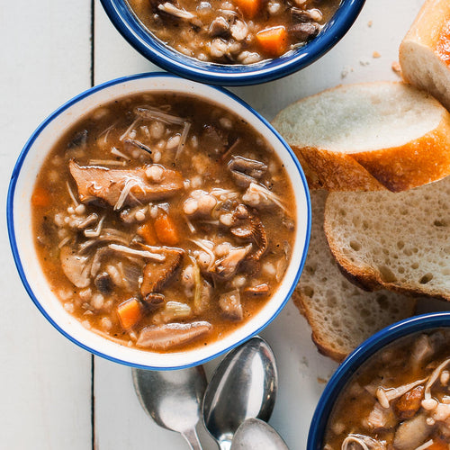 Bowls of wild mushroom barley soup served with bread on the side, with a spoon in one of the bowls.